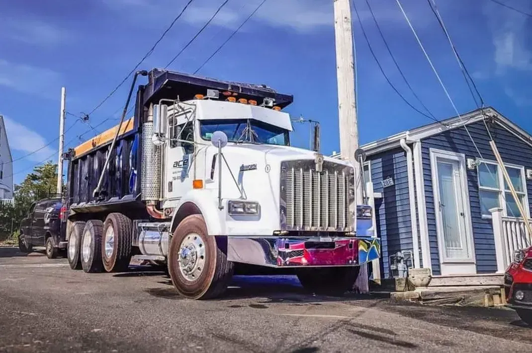 White dump truck on a street beside small houses under a blue sky