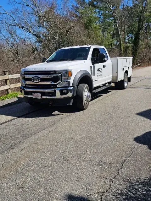 White Ford utility truck parked on a road beside a wooden fence and leafless trees