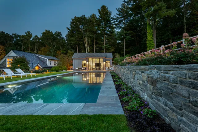 Evening view of a pool, pool house and dry-laid stone retaining wall