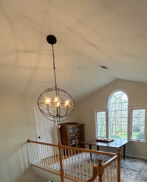 Looking down a staircase in a house with a chandelier and a reading area.