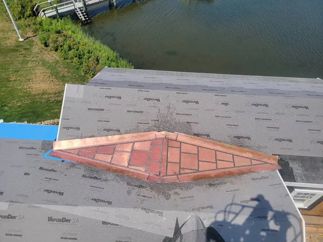 Custom red copper flat lock cricket on a waterfront roof in Centerville