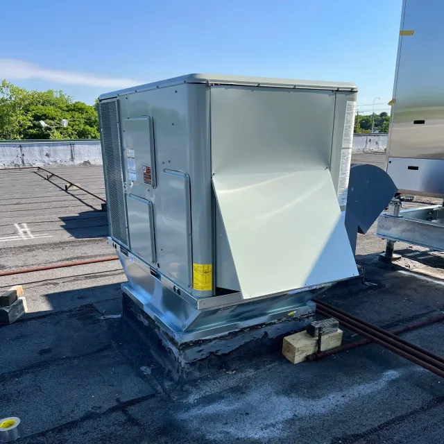 A rooftop with HVAC units and building materials, with trees in the background under a clear blue sky.