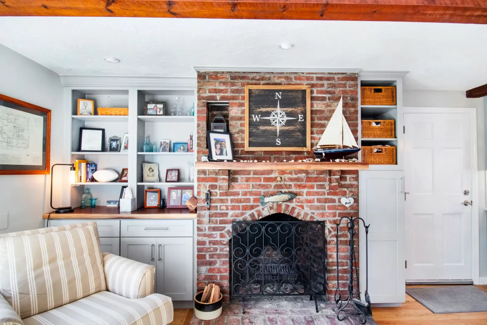 Fireplace with brick surround, built-in shelves, framed nautical artwork, and a model sailboat in a cozy living room.