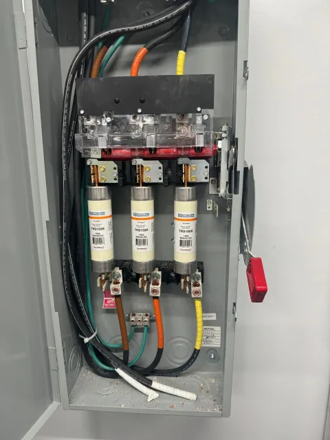 Electrical panel with three fuses, wires, and a red safety lock.