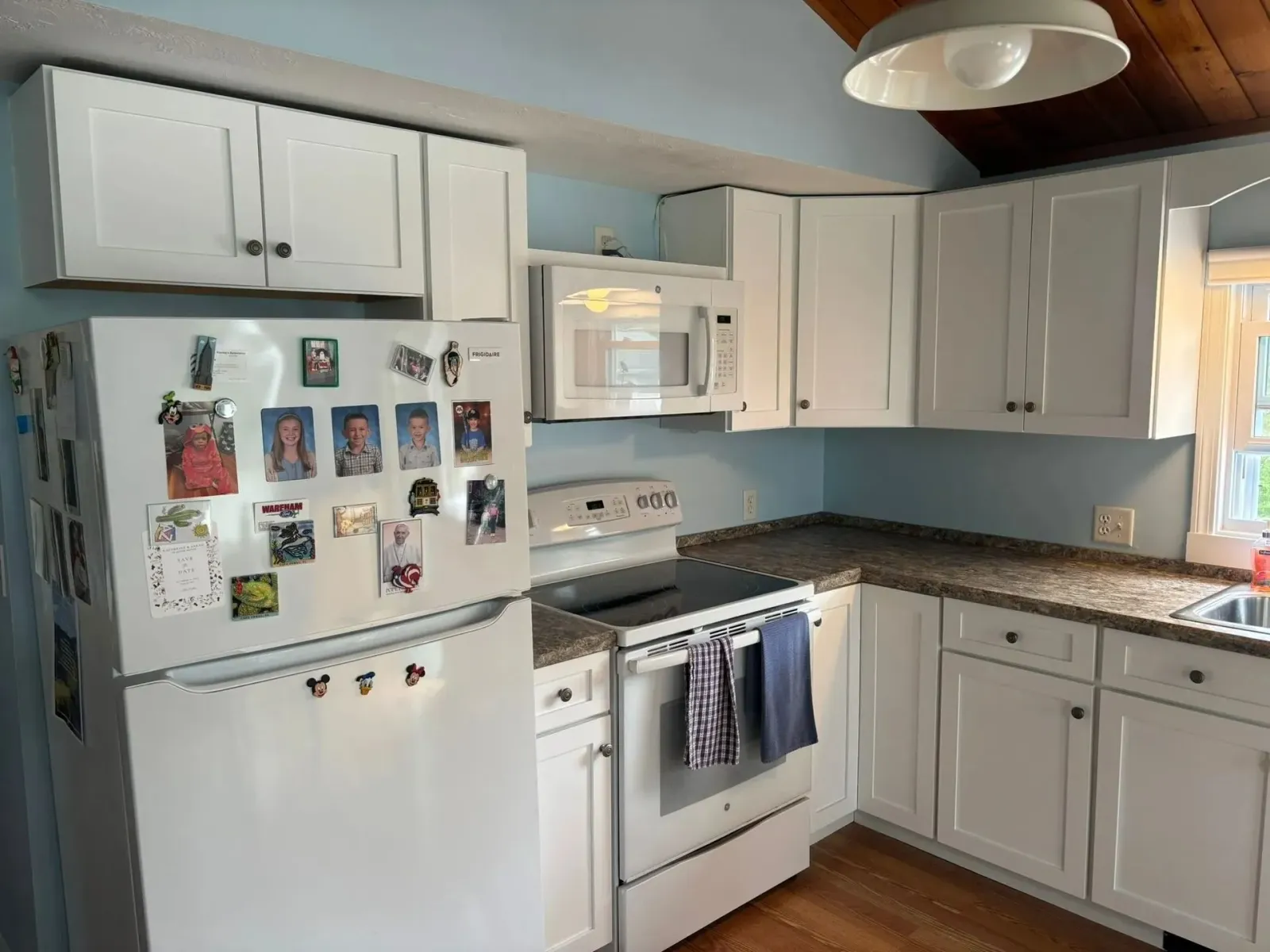 White kitchen with cabinets, refrigerator, microwave, and stove; light blue wall.