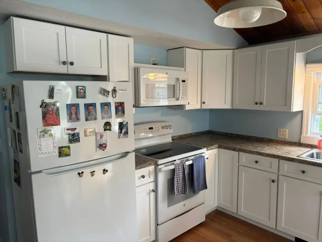 White kitchen with cabinets, refrigerator, microwave, and stove; light blue wall.
