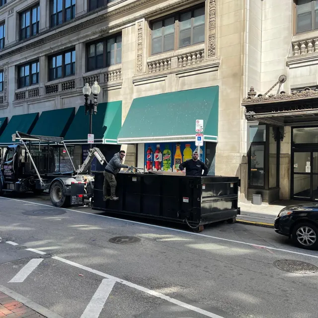 2 workers in a Buddy & Son Cleanouts dumpster in a city street