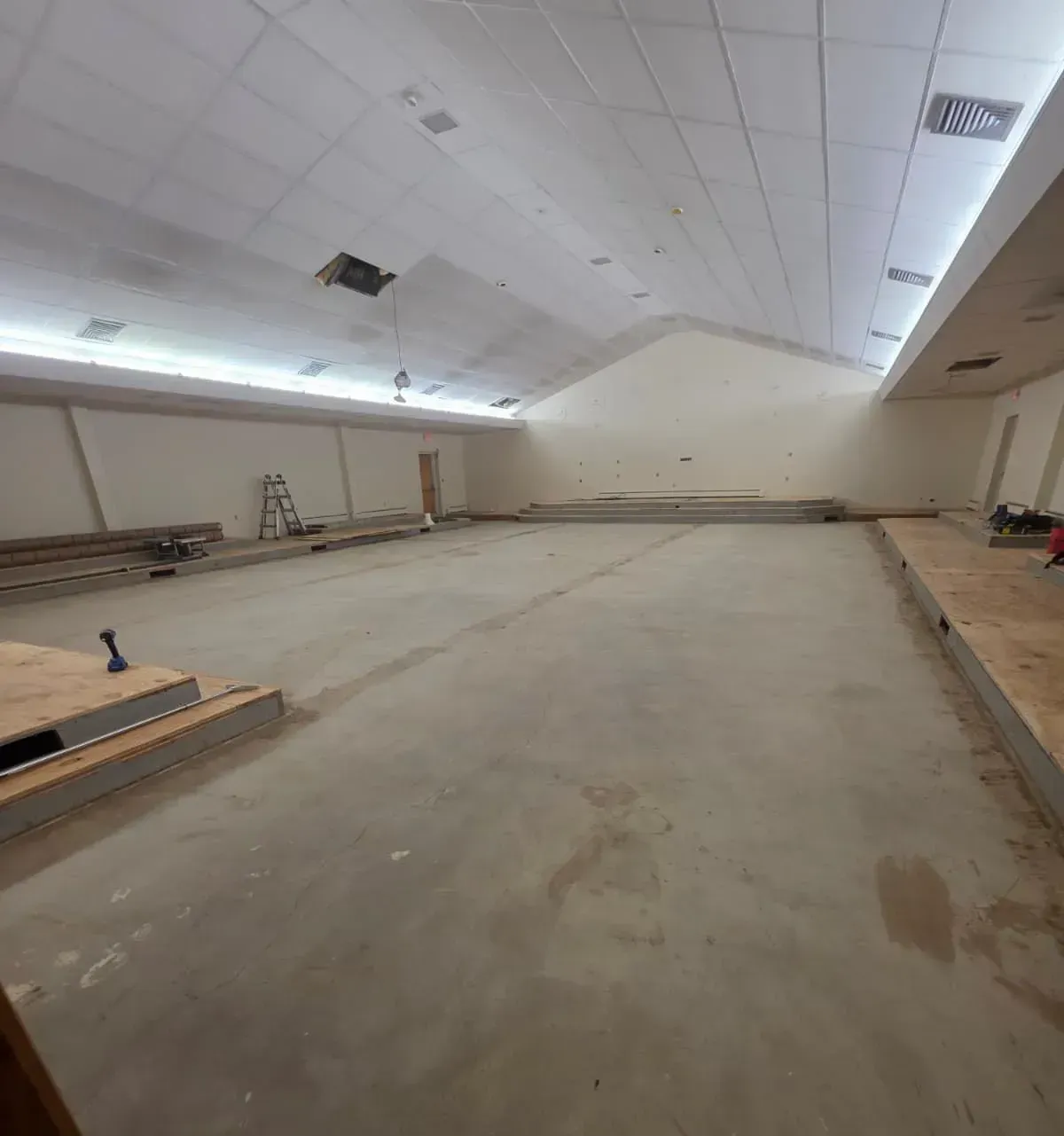 Empty unfinished room with concrete floor, white ceiling, and construction materials along the walls.