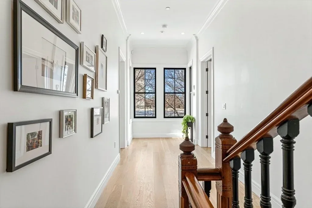 Bright hallway with white walls, black-framed windows, wooden staircase, and a small table with a potted plant near the window.