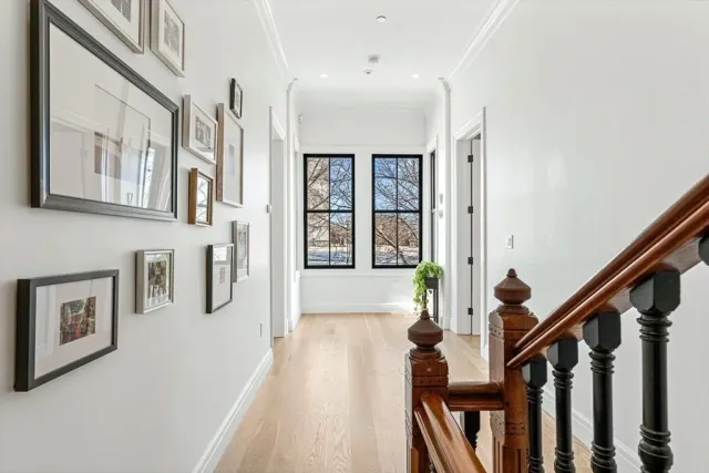Bright hallway with white walls, black-framed windows, wooden staircase, and a small table with a potted plant near the window.