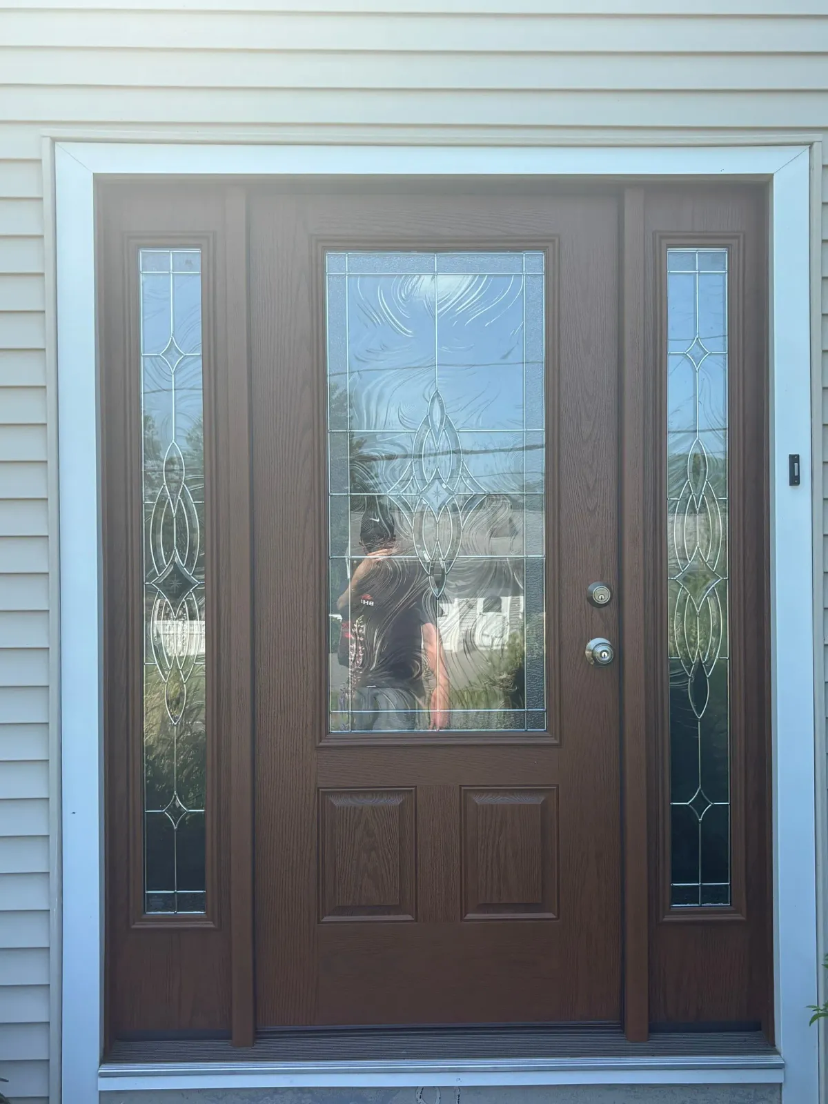 Brown front door with glass panels and sidelights. White trim, light siding.