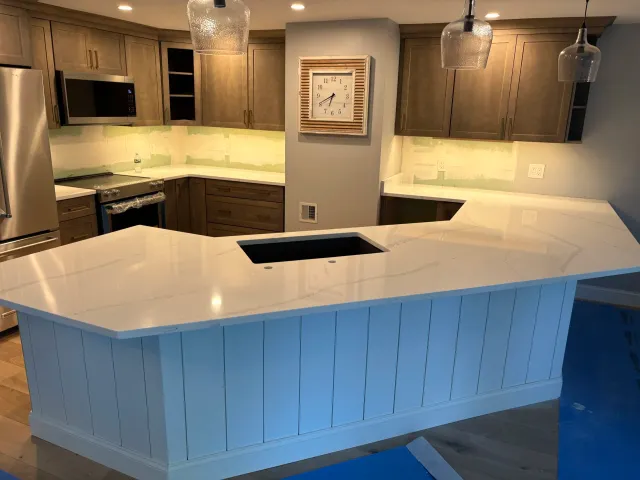 Modern kitchen with light-colored island, wooden cabinets, stainless steel appliances, and pendant lighting.