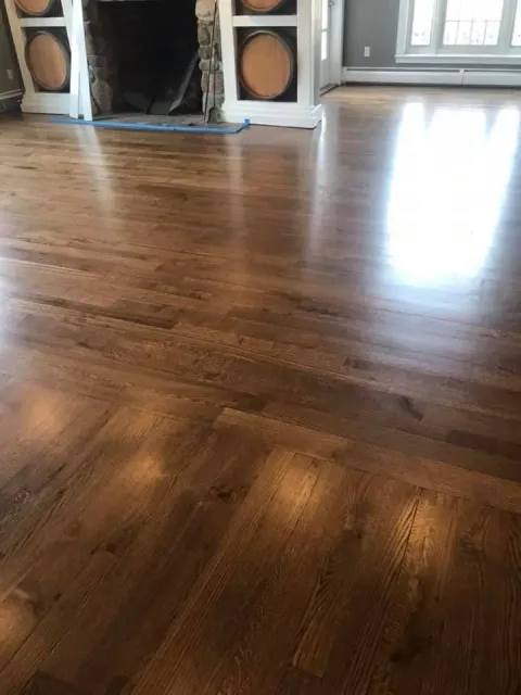 Hardwood floor in a bright room, reflecting light. Fireplace and windows in the background.