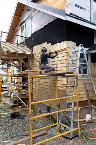 Worker on yellow scaffolding installing bamboo wall panels at a construction site
