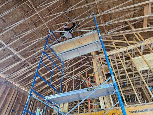 Person on scaffolding in a building under construction, working on ceiling wiring.