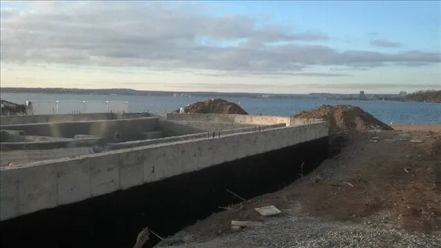 Coastal view with rocky formations and a concrete barrier under a cloudy sky.
