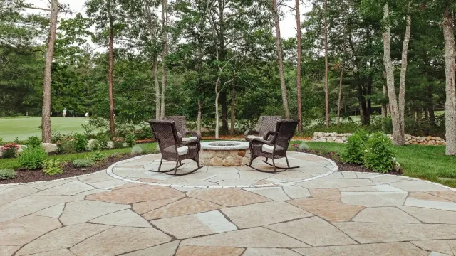 Stone patio, fire pit, and rocking chairs in backyard