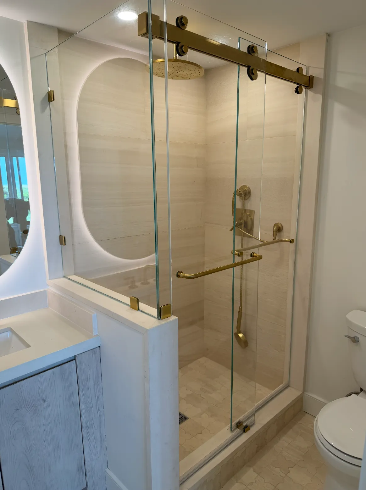 Bathroom with a glass shower enclosure, brass fixtures, a rain shower head, a handheld shower, and a white vanity with a sink.