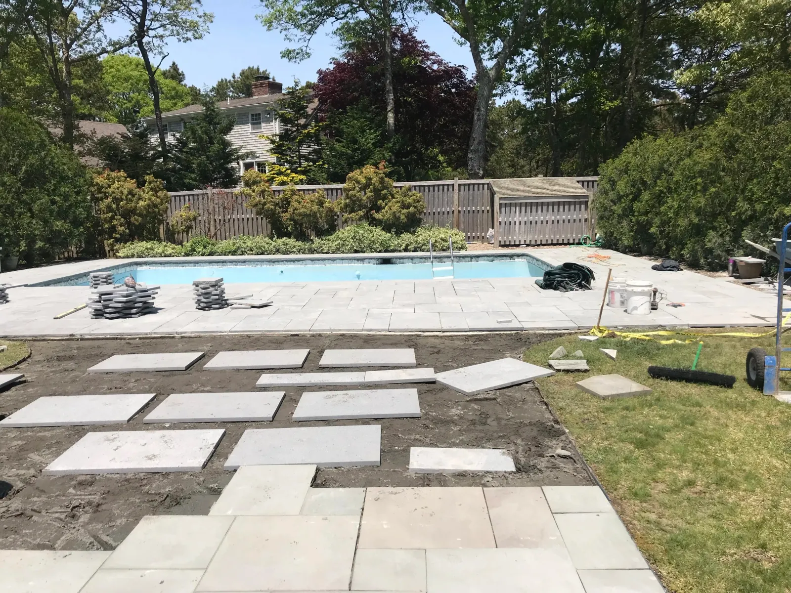 Backyard pool area under construction with paving stones and greenery.