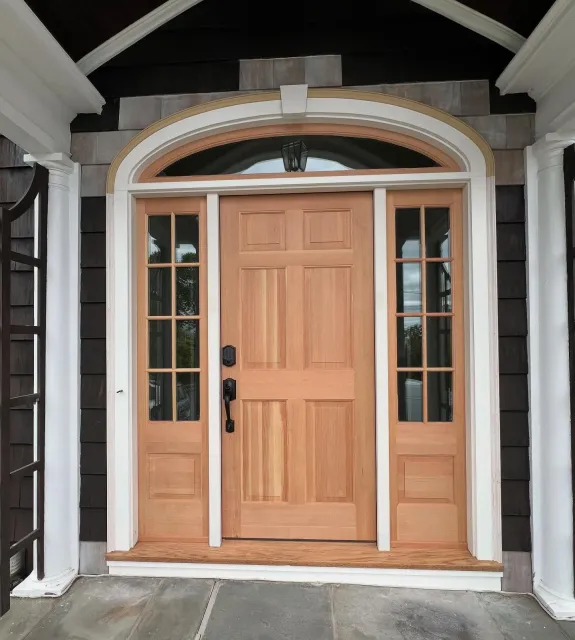 Front door with wooden panels, side glass panels, and an arched transom window, surrounded by black and white exterior trim.