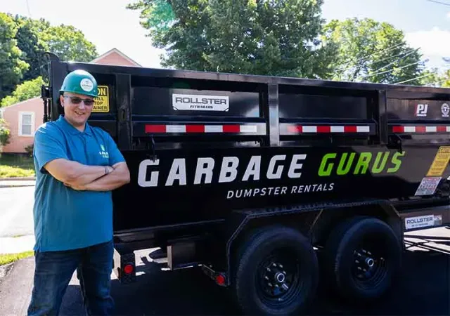 Man in blue shirt and green hard hat standing confidently next to Garbage Gurus dumpster rental truck, showcasing eco-friendly junk removal services.