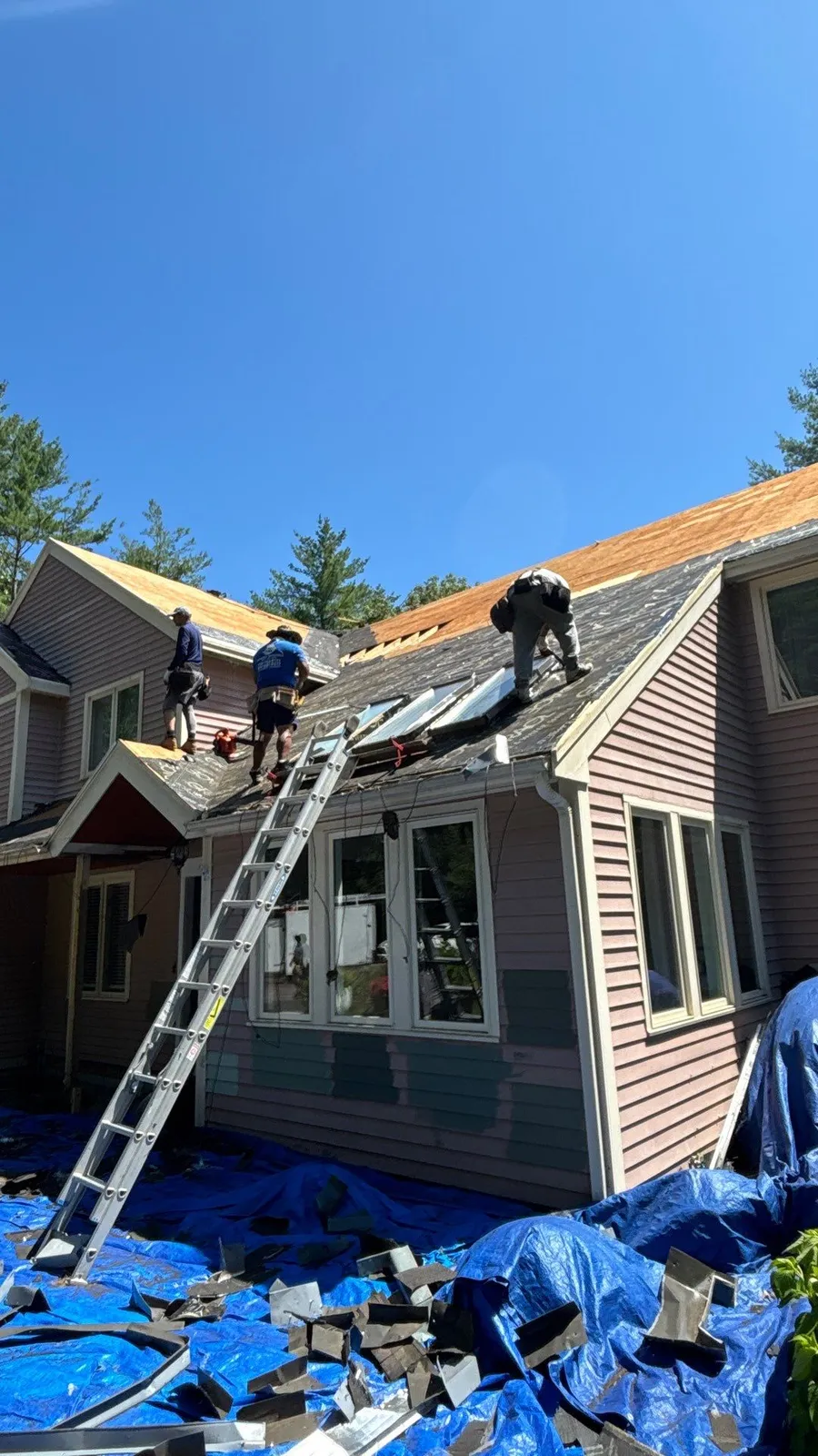 Workers repairing the roof of a house under a clear blue sky.
