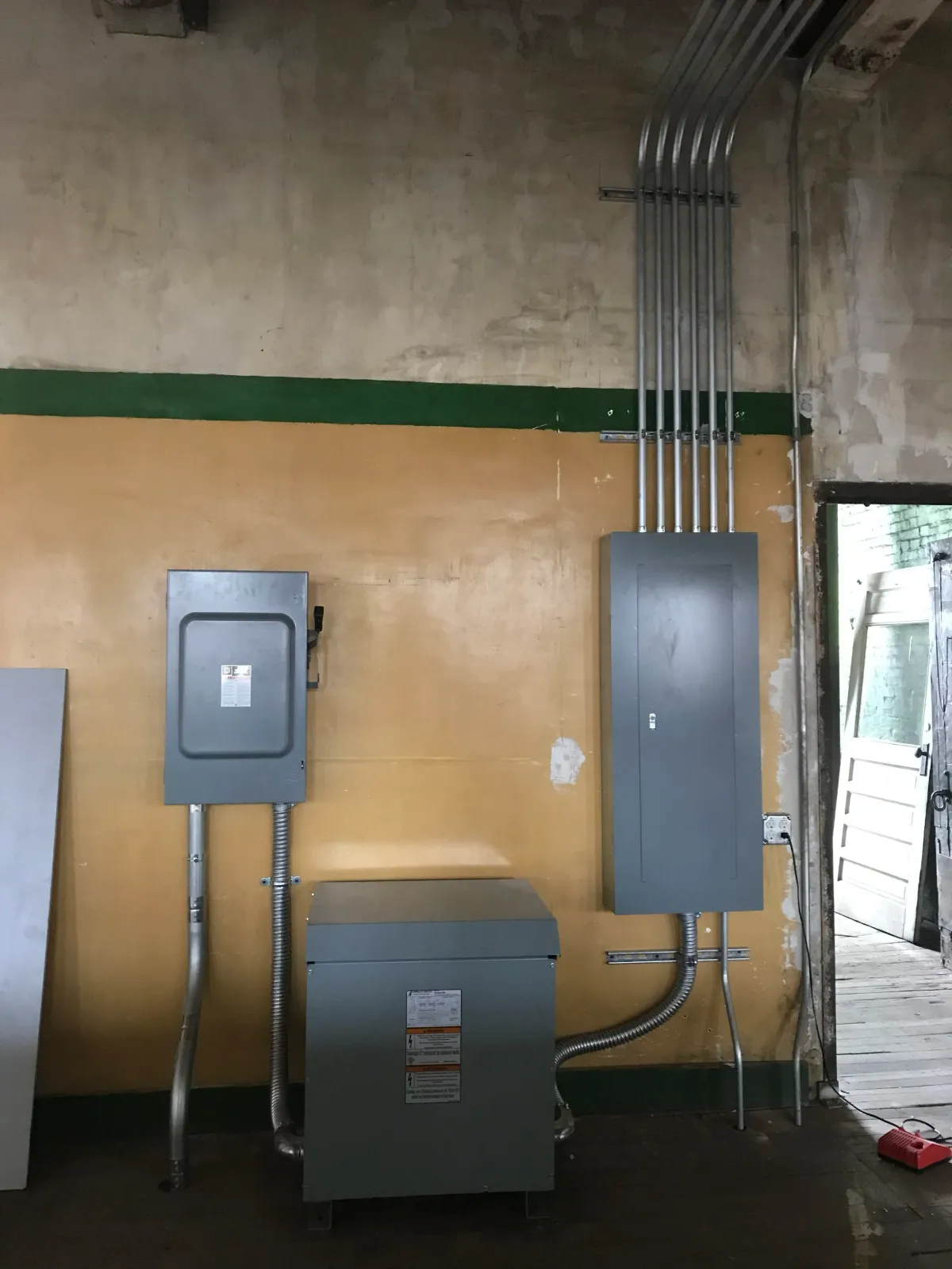 Electrical panels and conduit pipes mounted on a wall in a utility room.