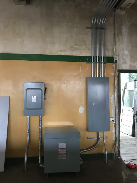 Electrical panels and conduit pipes mounted on a wall in a utility room.