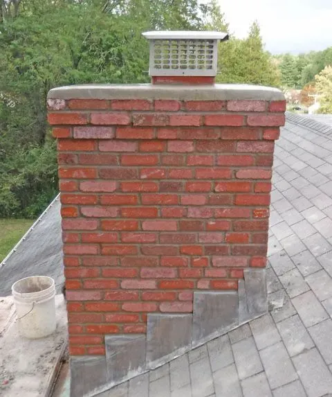 Red brick chimney on a shingled roof with a white metal vent cap