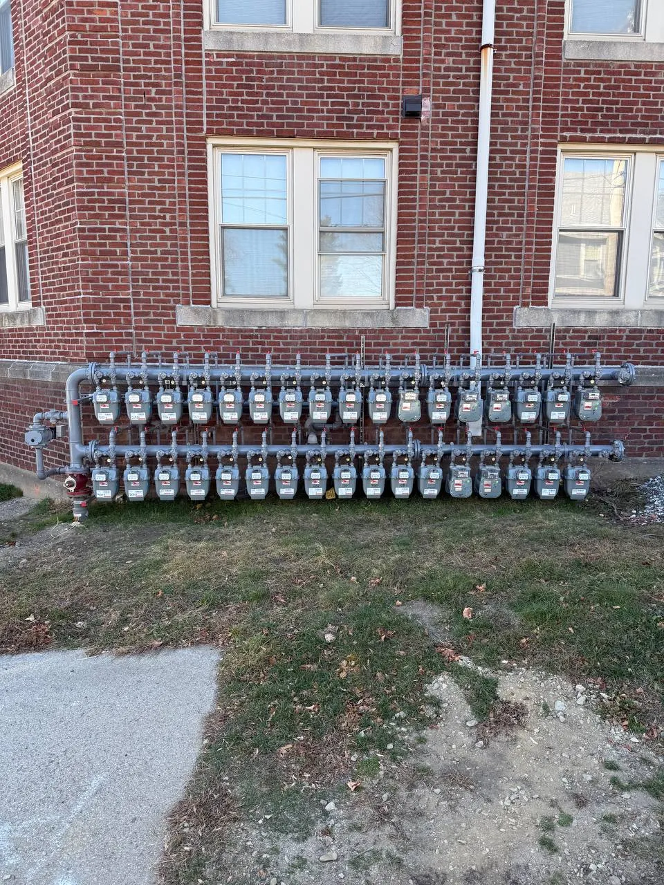 Bank of gas meters and piping mounted on an exterior brick building wall