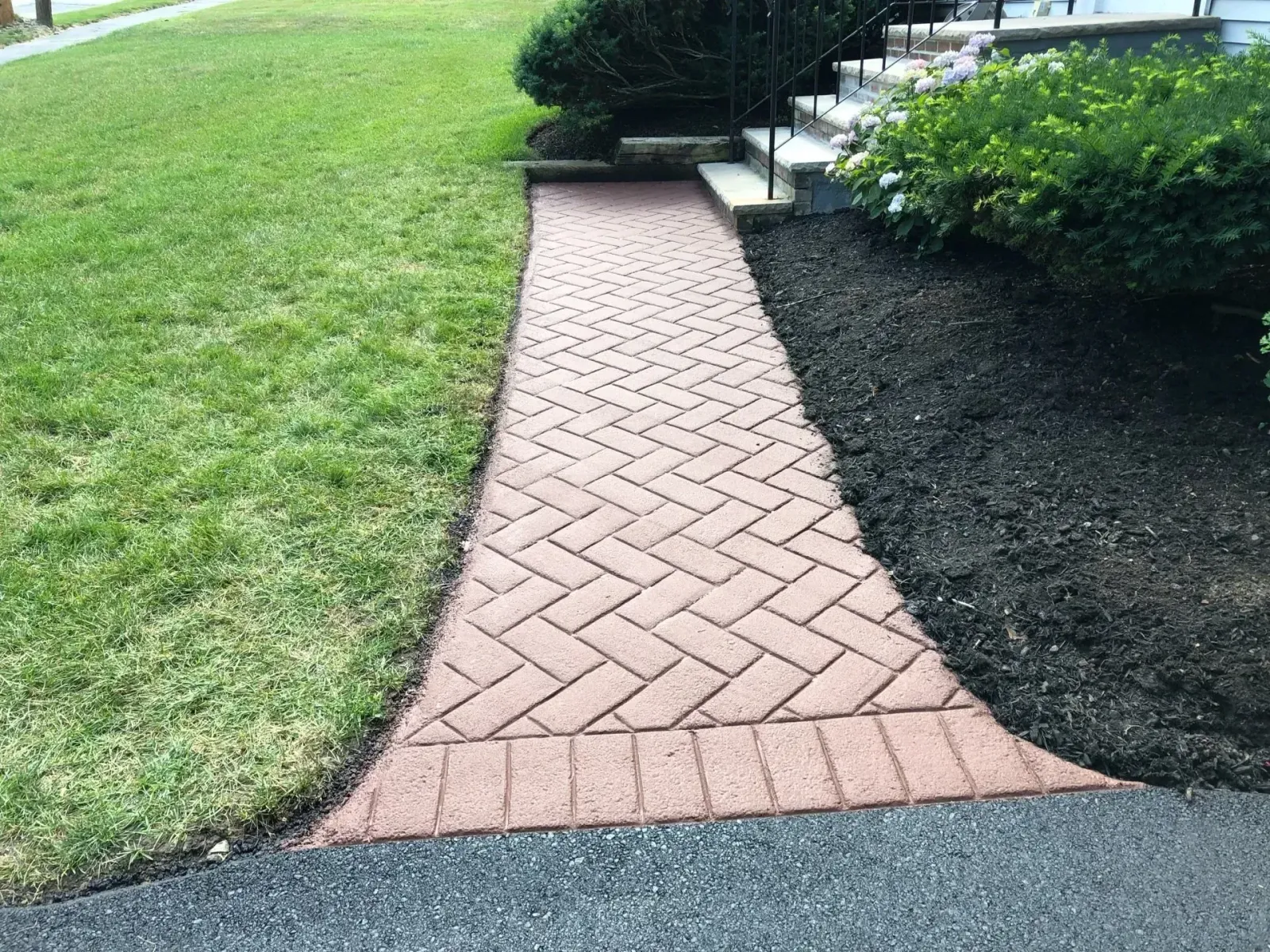 A brick walkway leading to a house with a herringbone pattern.