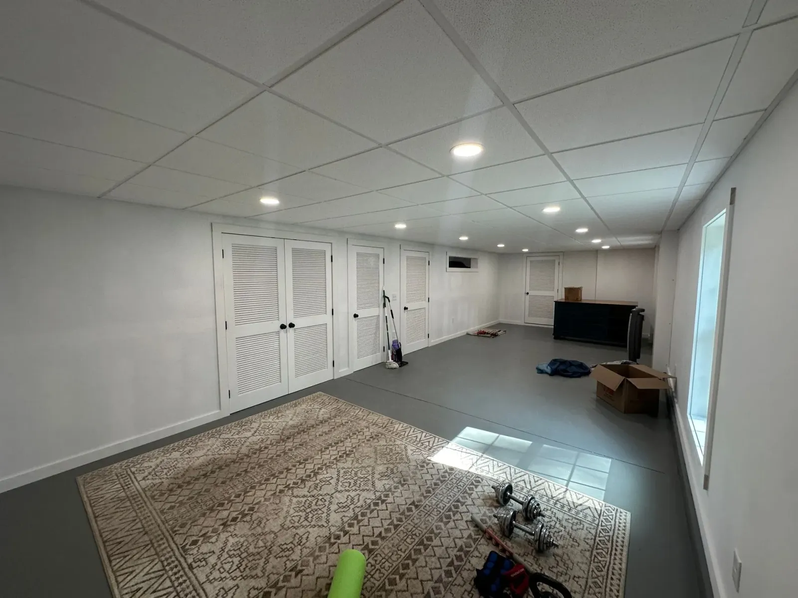 Empty finished basement with white walls, carpet, recessed lights, closet doors, and a window.