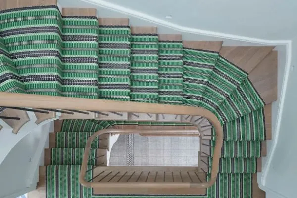 Overhead view of a winding staircase with a green and black striped stair runner installation. The runner adds pattern and color to the light wood stairs.