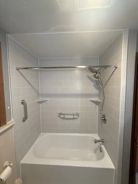 A white bathtub with silver fixtures, built-in shelves, and a gray surround.
