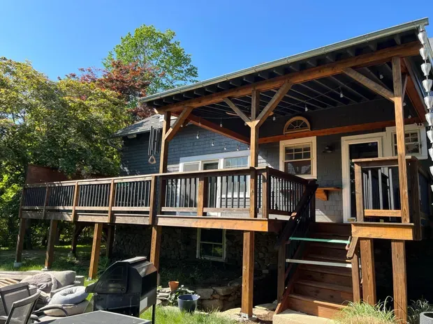 Wooden deck and patio attached to a gray house, with a grill on the lower level.