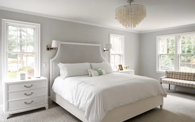 Photo of bedroom with large white bed, shell chandelier, and minimal decor - Woodland Builders, South Shore MA.