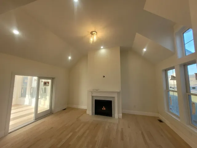 Light-filled living room with fireplace, vaulted ceiling, and sliding glass door. Blond hardwood floors, beige walls.