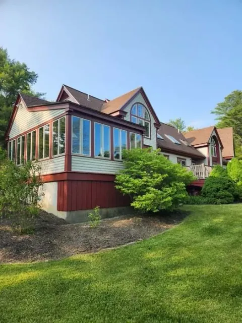 Large house with red siding and tall windows, set on a green lawn under a clear blue sky