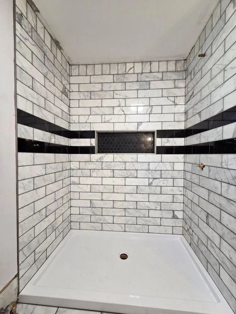 Empty tiled shower with white brick walls, black accent band, and white shower base.