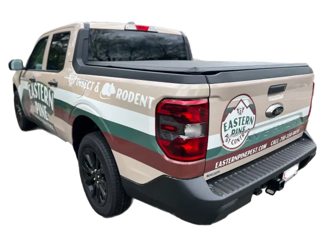 A beige and green pickup truck with "Eastern Pine Pest & Wildlife" branding and contact information displayed on the side and tailgate.