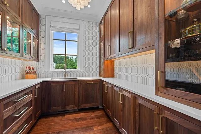 Dark wood pantry with white countertops, window, and decorative wallpaper.