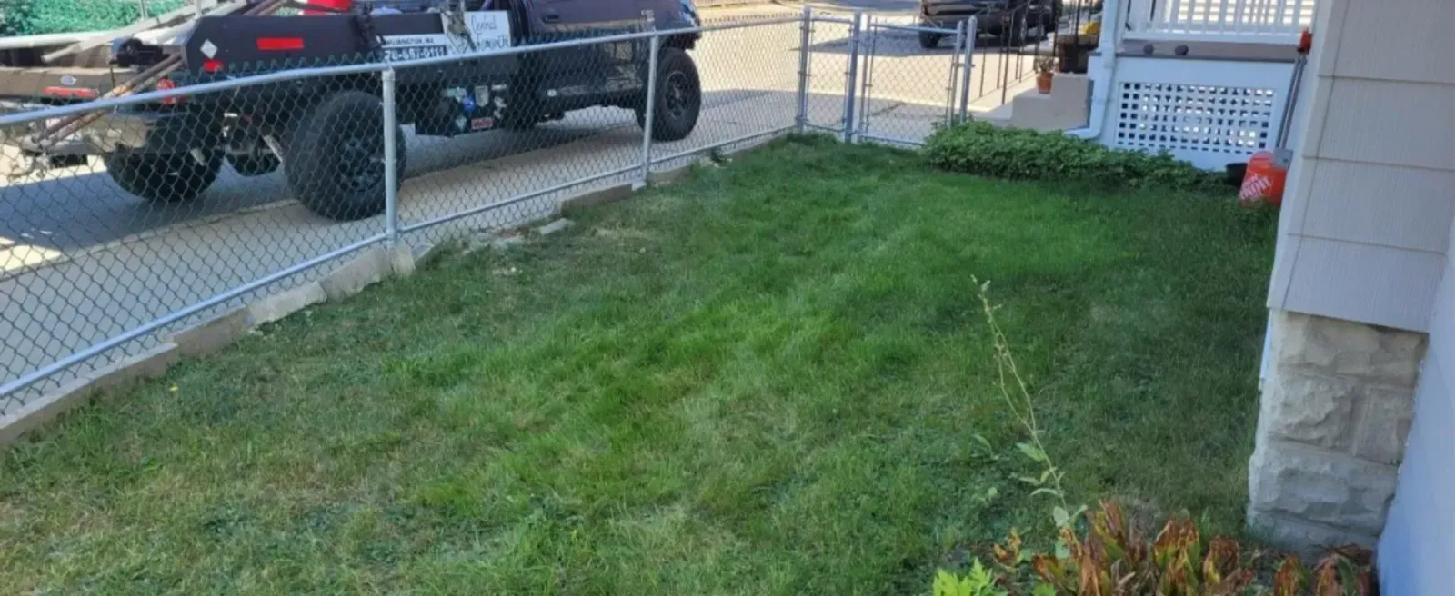 Front yard with patchy grass beside a chain-link fence and a parked black pickup truck.