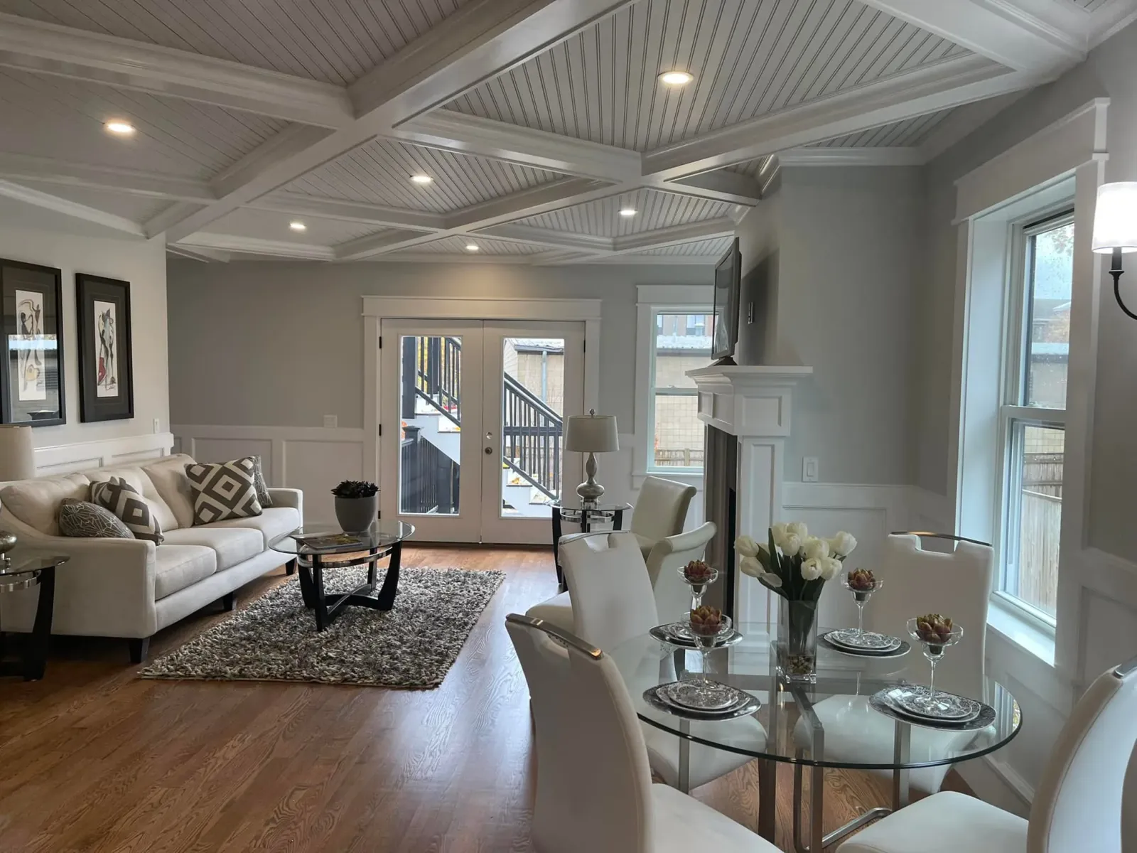 Open living room under a coffered ceiling, with fitted wall panels and a mantel beyond