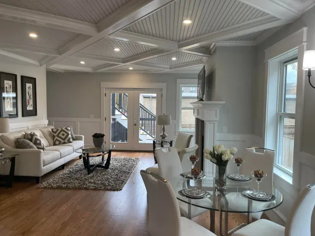 Open living room under a coffered ceiling, with fitted wall panels and a mantel beyond