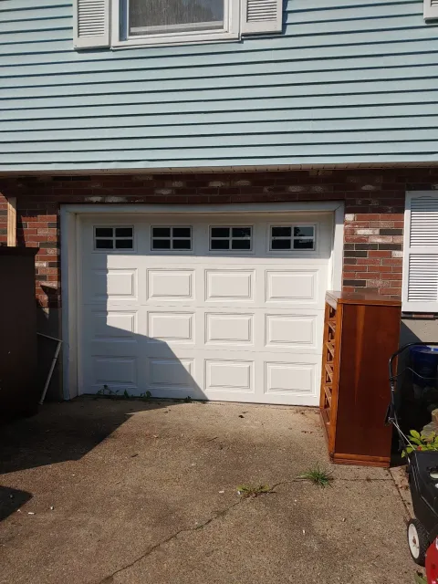 White garage door on a brick building, surrounded by discarded furniture and gravel.