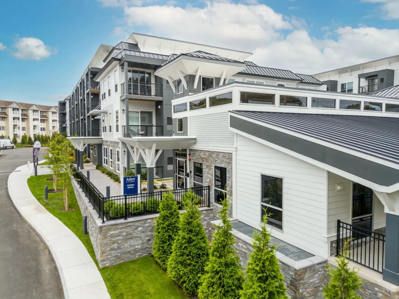 Exterior of modern apartment building with white and gray accents, lush greenery, and a curved sidewalk.