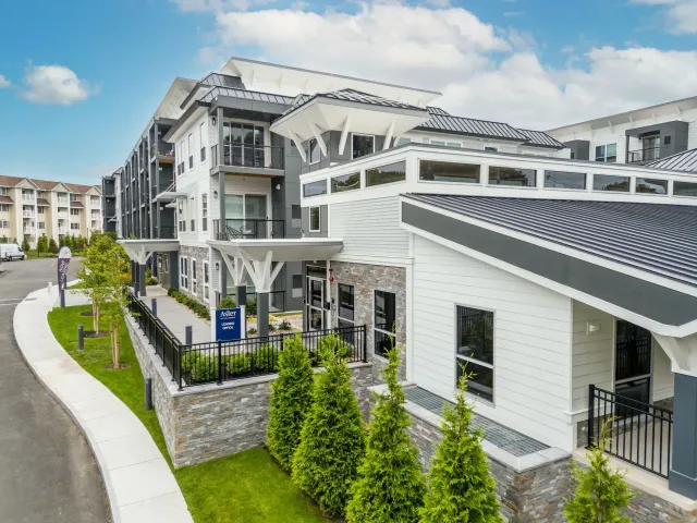 Exterior of modern apartment building with white and gray accents, lush greenery, and a curved sidewalk.