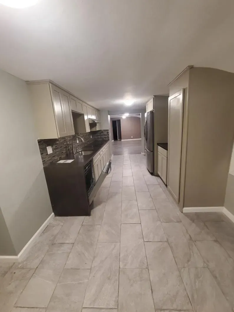 A kitchen with a refrigerator and a sink in a basement.