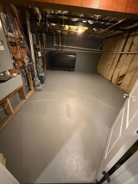 A view of a basement storage area with a freshly painted gray floor, exposed wall insulation, and utility equipment.