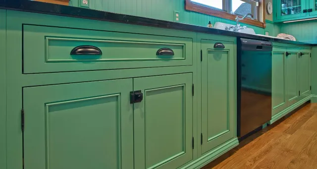 Mint-green kitchen cabinets with black handles along a countertop and wood floor